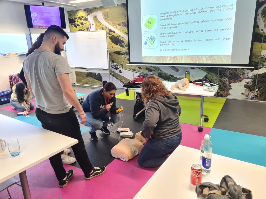 A trainer supervising learners as they practise first aid and using a defibrillator